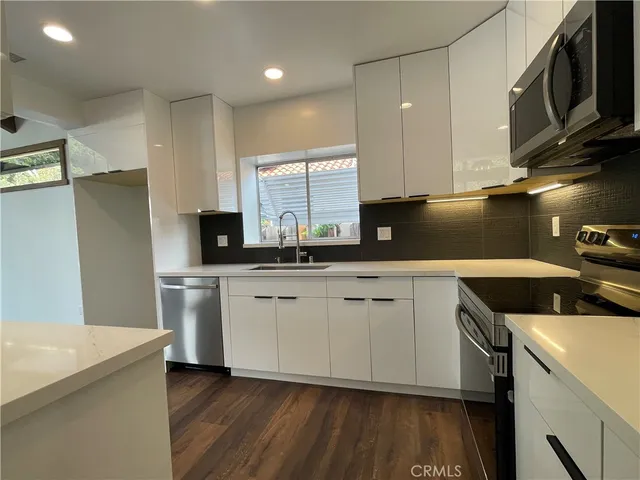a large kitchen with stainless steel appliances wooden floor and a large window