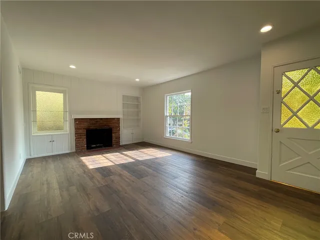 an empty room with wooden floor fireplace and windows