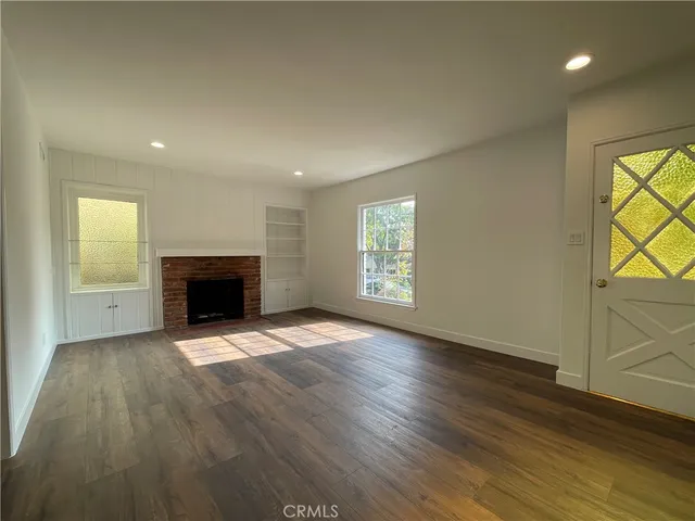 an empty room with wooden floor fireplace and windows