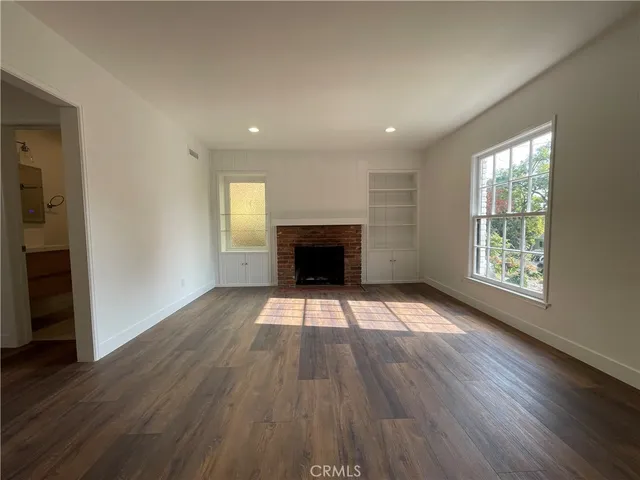 an empty room with wooden floor fireplace and windows