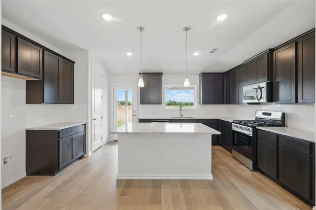a large kitchen with stainless steel appliances kitchen island granite countertop a stove a sink dishwasher and a refrigerator with wooden floor