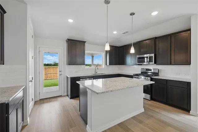 a large kitchen with stainless steel appliances granite countertop a sink dishwasher a stove and a refrigerator with wooden floor