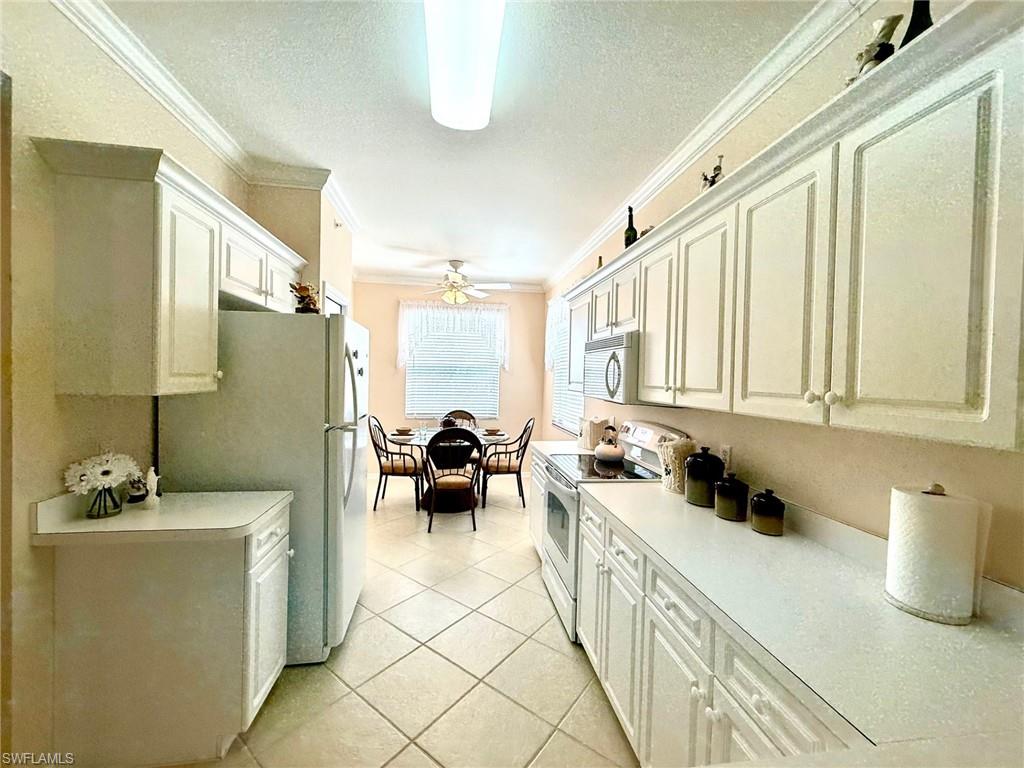 8450 Kingbird Loop, Unit 431 Estero, FL 33967 - Photo 13 of 47 Kitchen featuring white appliances, ornamental molding, light countertops, a textured ceiling, and white cabinetry