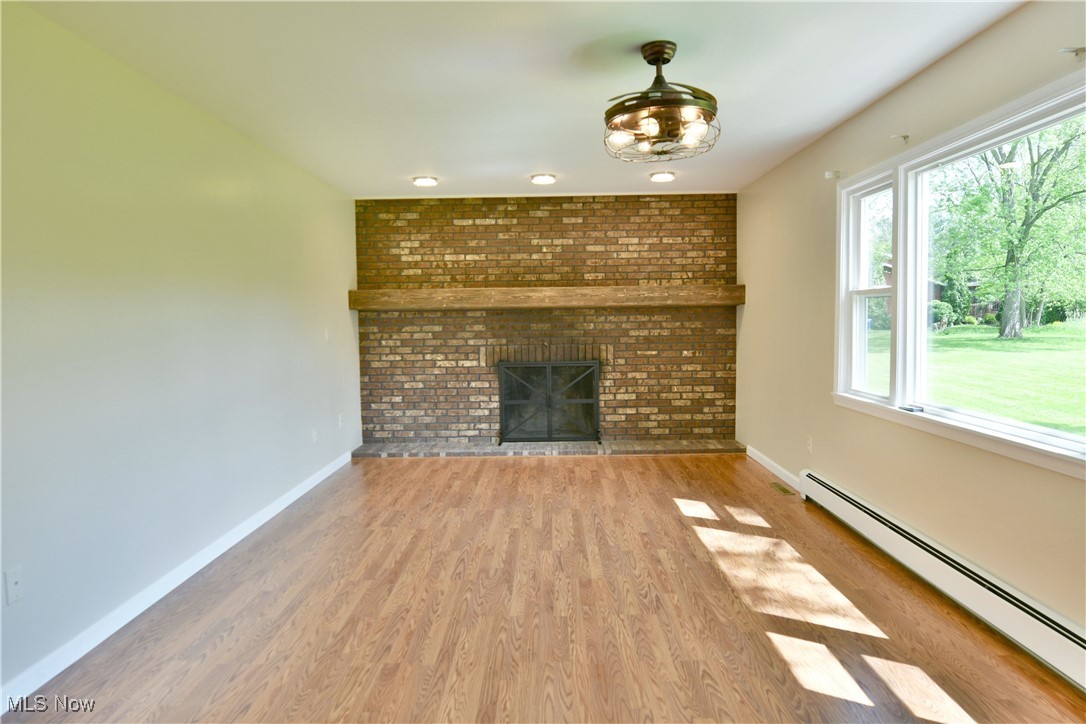 2153 Stillwagon Road Southeast Warren, OH 44484 - Photo 24 of 50 Unfurnished living room with a baseboard radiator, baseboards, wood finished floors, and a brick fireplace