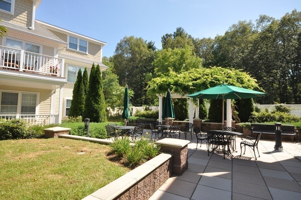 95 Conant Street, Unit 304 Concord, MA 01742 - Photo 22 of 23 a view of a patio with table and chairs under an umbrella with large trees