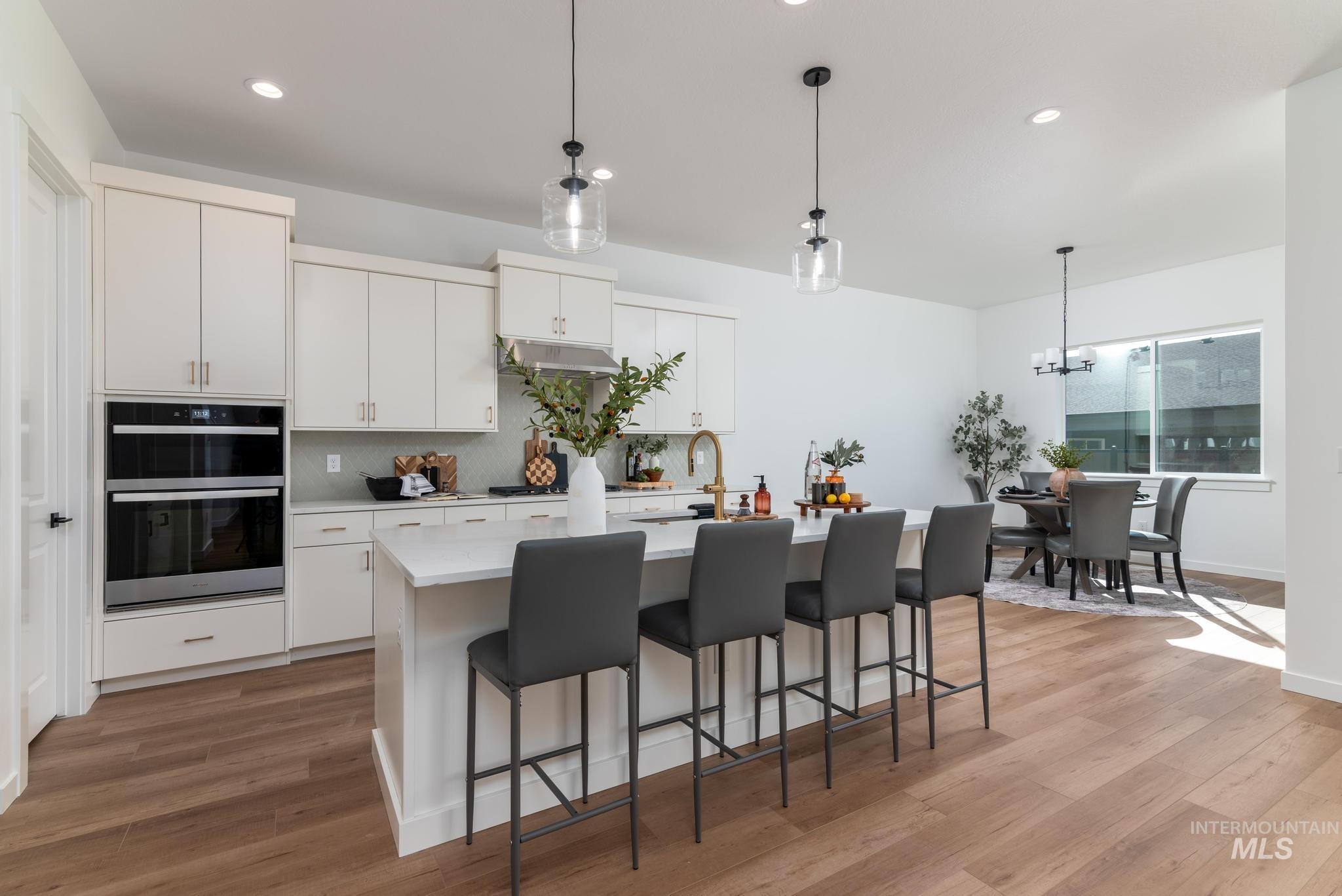 5402 Juliet Rose Avenue Caldwell, ID 83607 - Photo 4 of 20 Gourmet kitchen featuring white shaker cabinetry, stainless steel appliances, a center island with pendant lighting, and wood-finish flooring