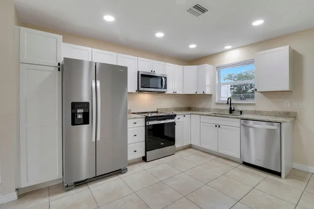 a kitchen with granite countertop white cabinets appliances a sink and a window