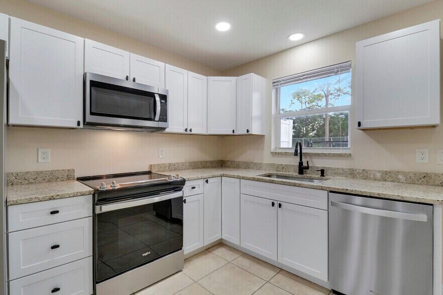 2777 Southeast Normand Street Stuart, FL 34997 - Photo 5 of 14 a kitchen with granite countertop white cabinets appliances a sink and a window