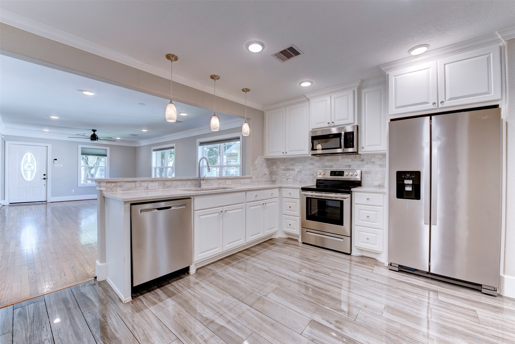 109 Dresden Street Houston, TX 77012 - Photo 15 of 43 This photo showcases a modern, open-concept kitchen and living area. The kitchen features stainless steel appliances, white cabinetry, and a sleek backsplash. It flows into a bright living space with hardwood floors and large windows, offering plenty of natural light.