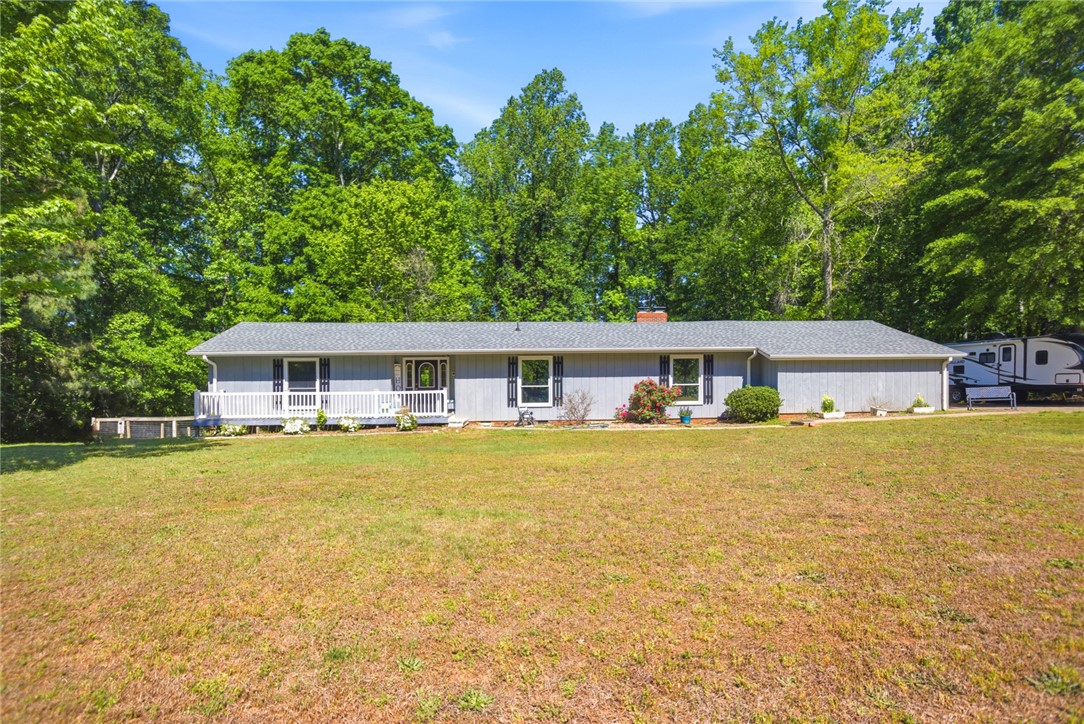 A classic ranch home offers a welcoming front porch with white railings, set against a backdrop of mature trees.