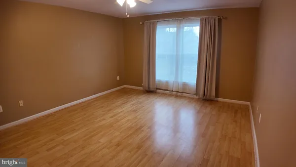 an empty room with wooden floor and windows with curtains