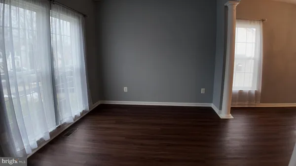 an empty room with wooden floor and windows with curtains