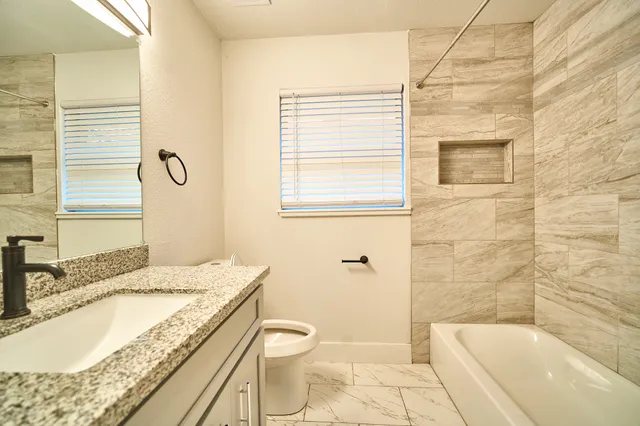 a bathroom with a granite countertop sink a toilet and bathtub