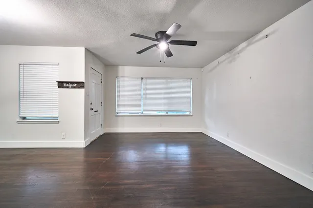 an empty room with wooden floor chandelier fan and windows