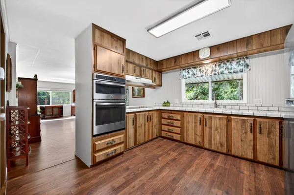 a kitchen with stainless steel appliances a large window a wooden floor and fence