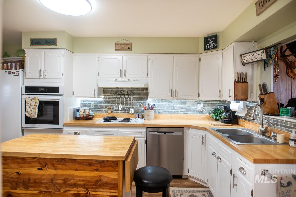 733 Pringle Road Weiser, ID 83672 - Photo 16 of 46 Kitchen with butcher block countertops, tasteful backsplash, white appliances, and white cabinetry