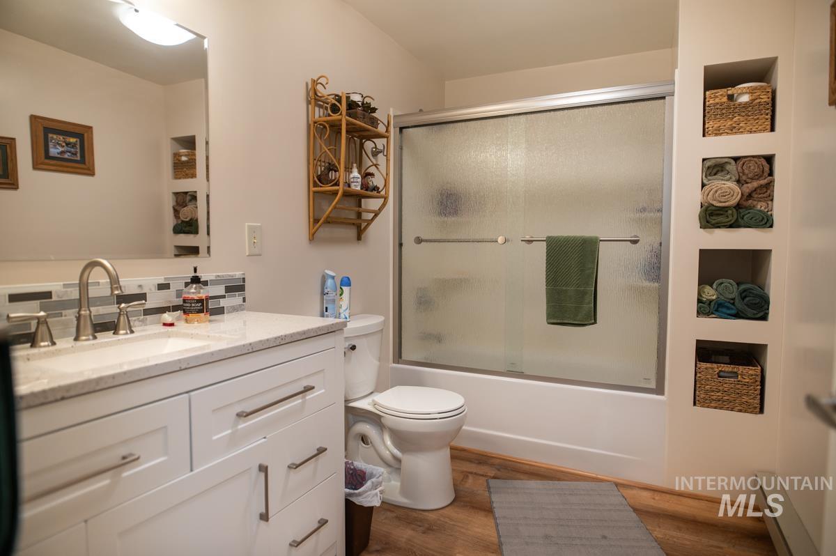 733 Pringle Road Weiser, ID 83672 - Photo 26 of 46 Full bath featuring vanity, combined bath / shower with glass door, wood finished floors, baseboard heating, and decorative backsplash