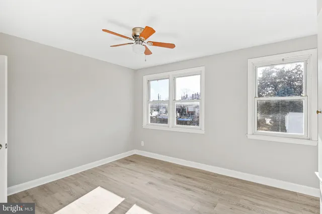 a view of an empty room with wooden floor and a ceiling fan