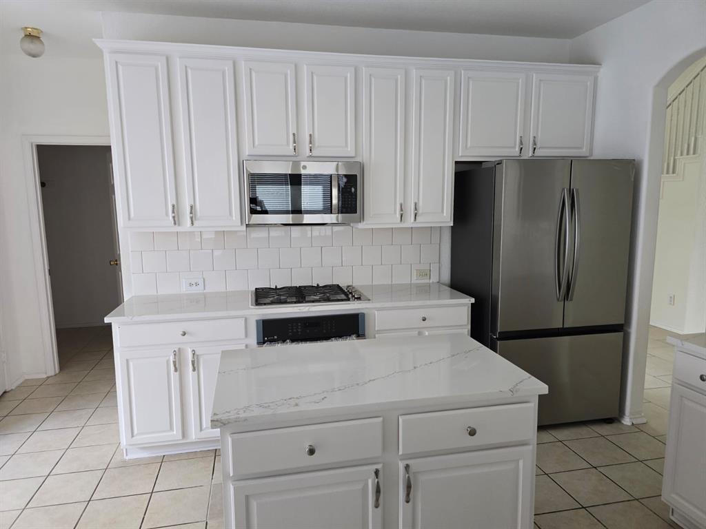 4325 Ridge Point Lane Plano, TX 75024 - Photo 6 of 11 Kitchen featuring tasteful backsplash, light tile patterned floors, stainless steel appliances, white cabinets, and a center island
