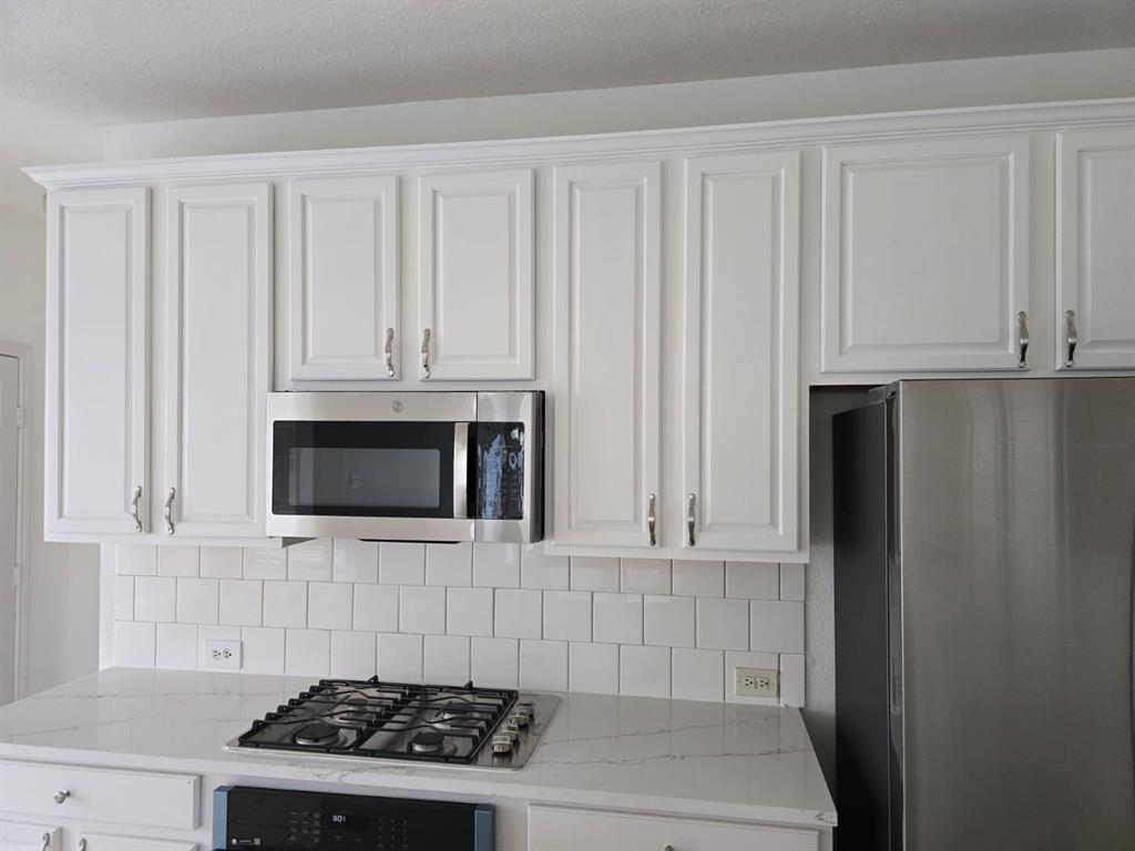 4325 Ridge Point Lane Plano, TX 75024 - Photo 7 of 11 Kitchen featuring white cabinetry, light stone counters, appliances with stainless steel finishes, and decorative backsplash