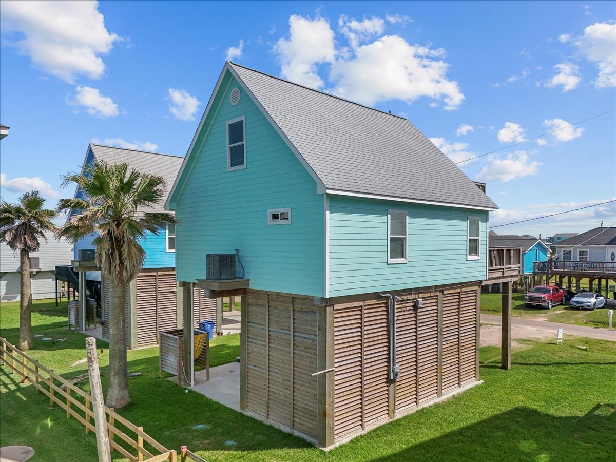 130 Beachcomber Avenue Surfside Beach, TX 77541 - Photo 29 of 33 This is a charming elevated coastal home with a bright sea glass teal exterior, situated on a grassy lot. It features a fenced area, covered parking underneath, and is surrounded by scenic palm trees, perfect for those seeking a beachside lifestyle.