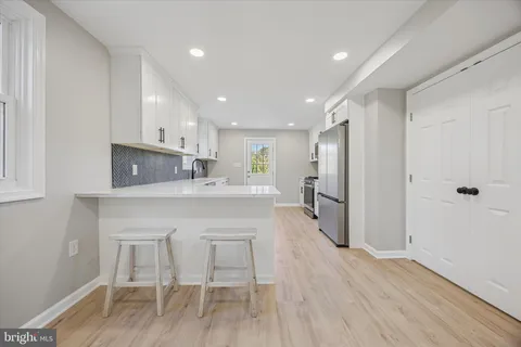 a view of an empty room with kitchen and wooden floor