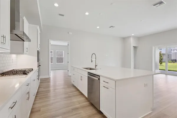 a view of an empty room with wooden floor and a kitchen