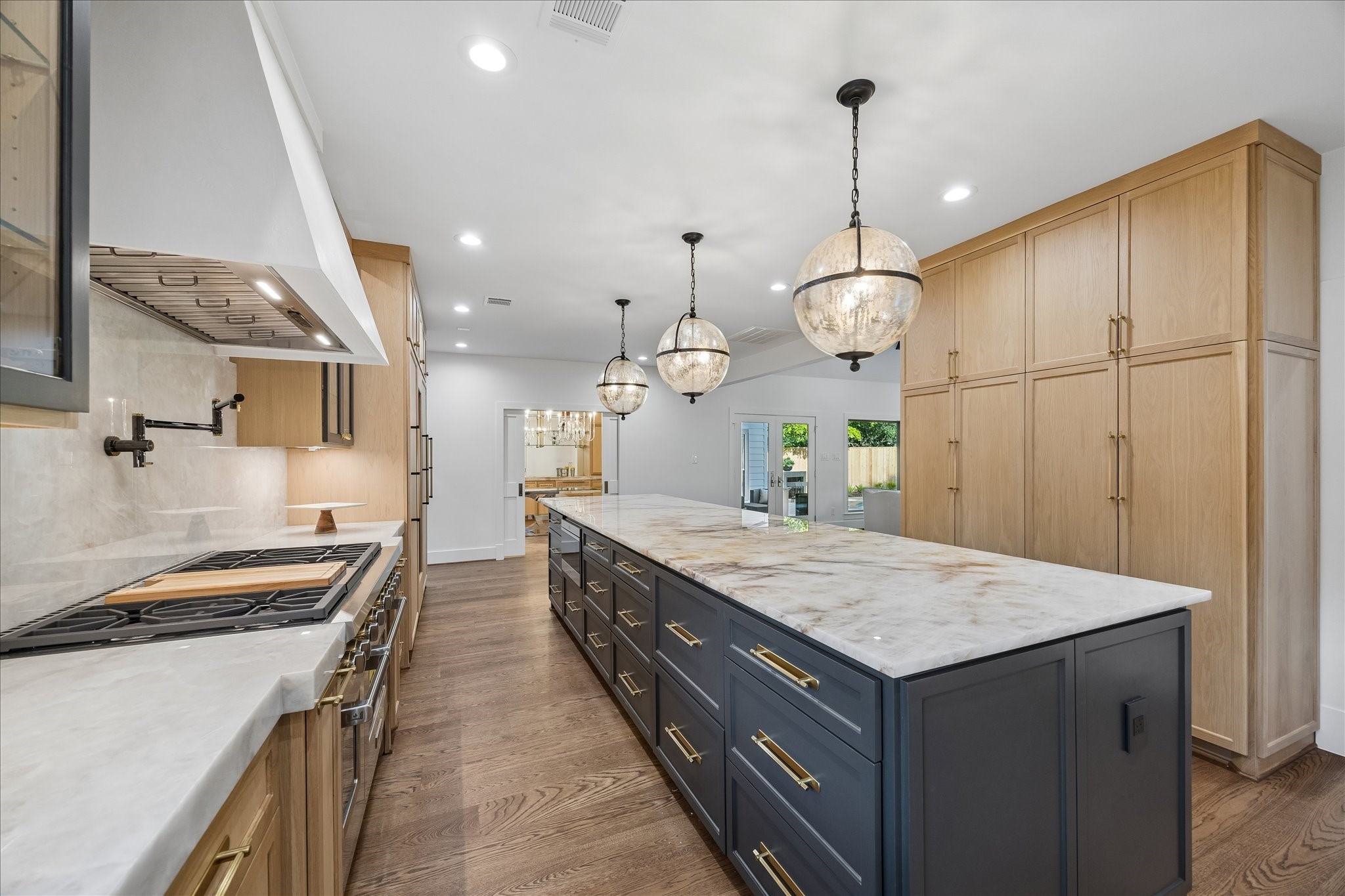 620 Stoneleigh Drive Houston, TX 77079 - Photo 13 of 39 The kitchen features Crystallo Super White quartzite countertops with a striking 3” mitered edge and full backsplash, paired with warm oak cabinetry for a clean, elevated look. Cabinetry along the right wall is thoughtfully designed with pull-out drawers for pantry and additional storage, while a separate pantry is conveniently located off the utility room.