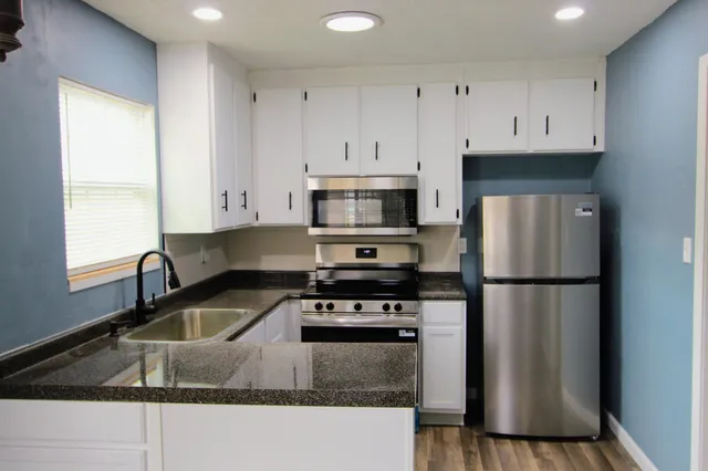 a kitchen with granite countertop a refrigerator a stove a sink and white cabinets with wooden floor