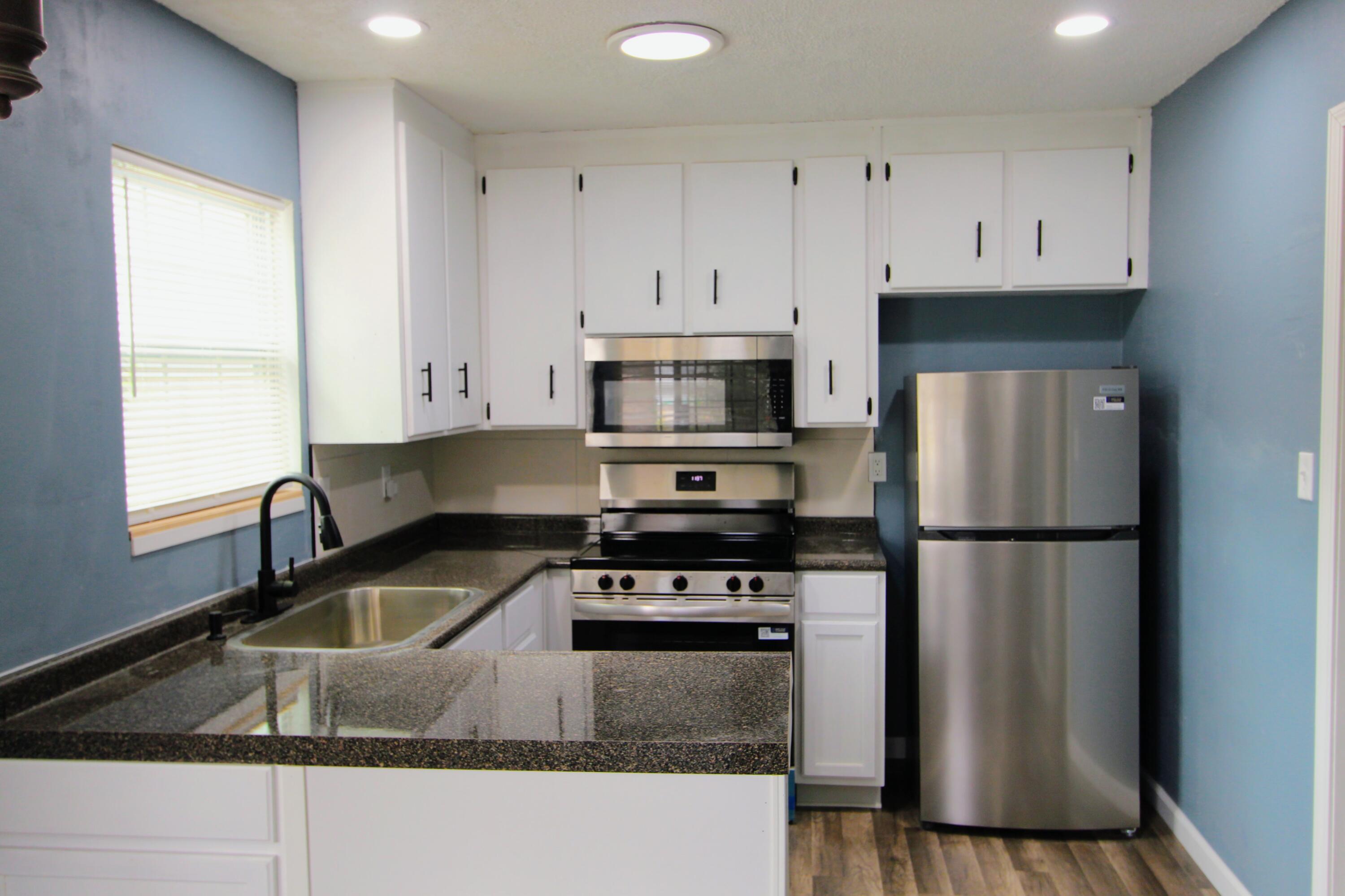 8250 Kause Road Pensacola, FL 32506 - Photo 12 of 28 a kitchen with granite countertop a refrigerator a stove a sink and white cabinets with wooden floor