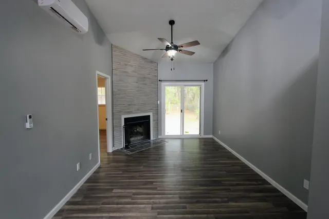 a view of an empty room with wooden floor fireplace and a window