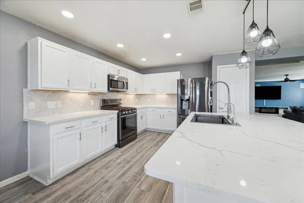 a kitchen with granite countertop a refrigerator oven a sink dishwasher and white cabinets with wooden floor