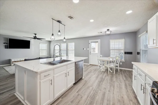 a kitchen with stainless steel appliances a stove top oven a sink dishwasher and white cabinets with wooden floor