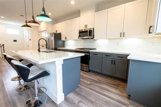 a kitchen with stainless steel appliances granite countertop a refrigerator a sink dishwasher a stove and white cabinets with wooden floor