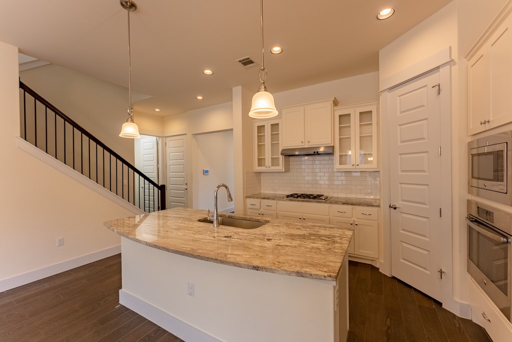 13008 Armaga Springs Road Austin, TX 78727 - Photo 10 of 33 Kitchen with dark wood-style floors, light stone countertops, stainless steel appliances, glass fronted cabinets, and a center island with sink