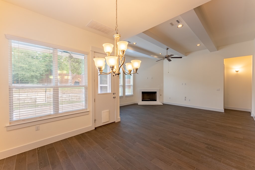 13008 Armaga Springs Road Austin, TX 78727 - Photo 12 of 33 Unfurnished living room with suspended lighting, a ceiling fan, a fireplace with raised hearth, dark wood-style flooring, and beamed ceiling