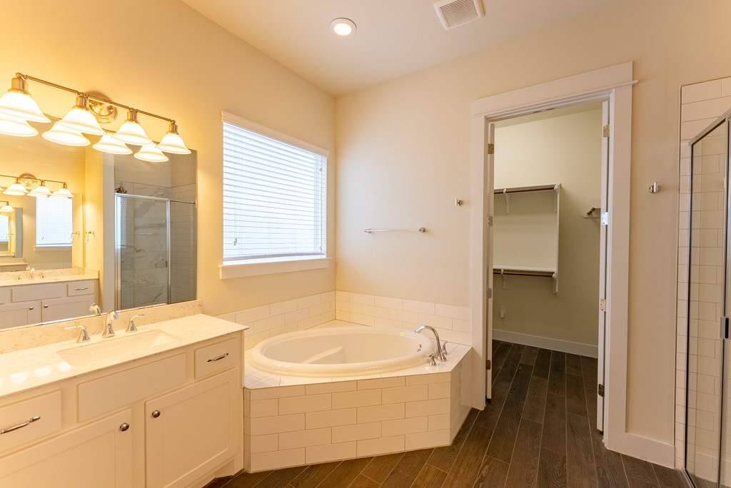 13008 Armaga Springs Road Austin, TX 78727 - Photo 17 of 33 Bathroom with a shower stall, vanity, a garden tub, dark wood-style flooring, and a spacious closet