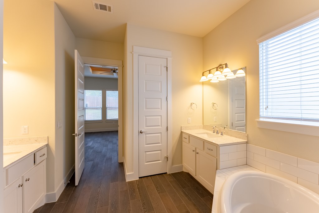 13008 Armaga Springs Road Austin, TX 78727 - Photo 18 of 33 Bathroom featuring dark wood finished floors, two vanities, a garden tub, and a ceiling fan