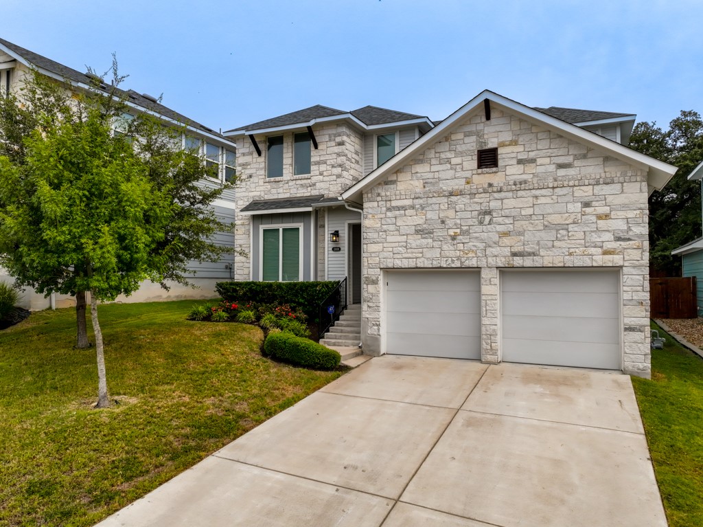 13008 Armaga Springs Road Austin, TX 78727 - Photo 2 of 33 View of front facade featuring stone siding, driveway, a front yard, and an attached garage