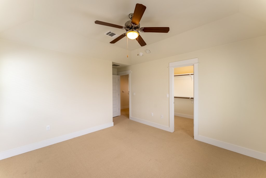 13008 Armaga Springs Road Austin, TX 78727 - Photo 24 of 33 Unfurnished bedroom featuring light colored carpet, a walk in closet, and a ceiling fan