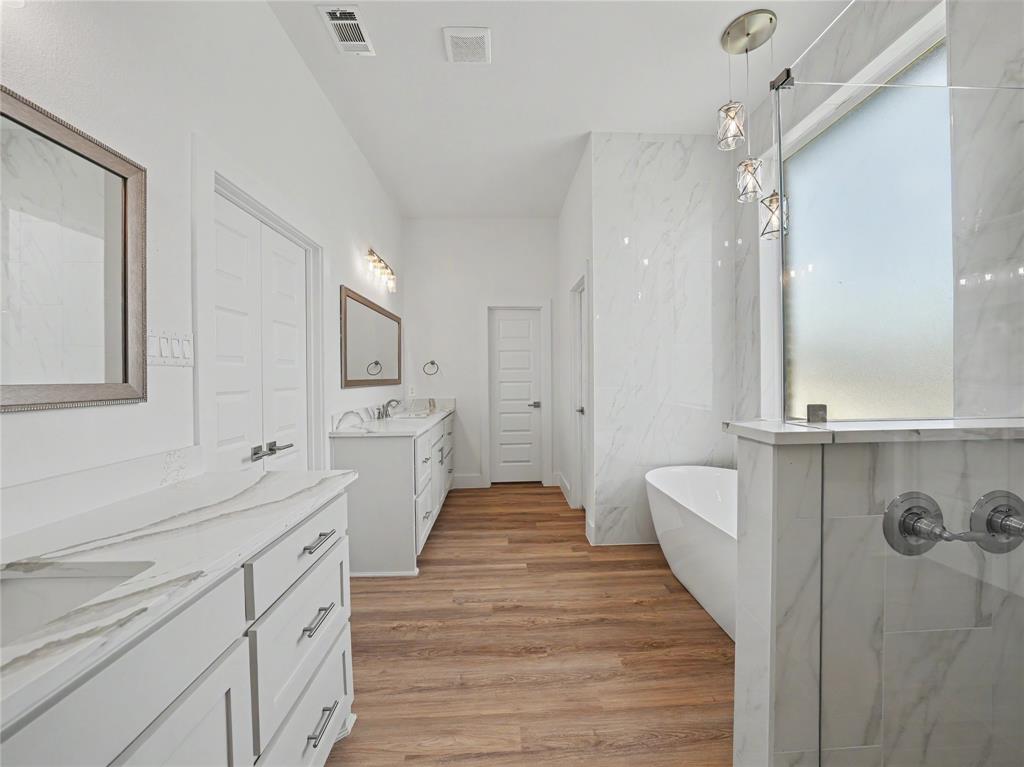 328 Slimp Bluff Azle, TX 76020 - Photo 19 of 30 Contemporary bathroom featuring a freestanding tub, a walk-in shower with a frosted glass panel, and dual vanities with white cabinetry and light-toned countertops
