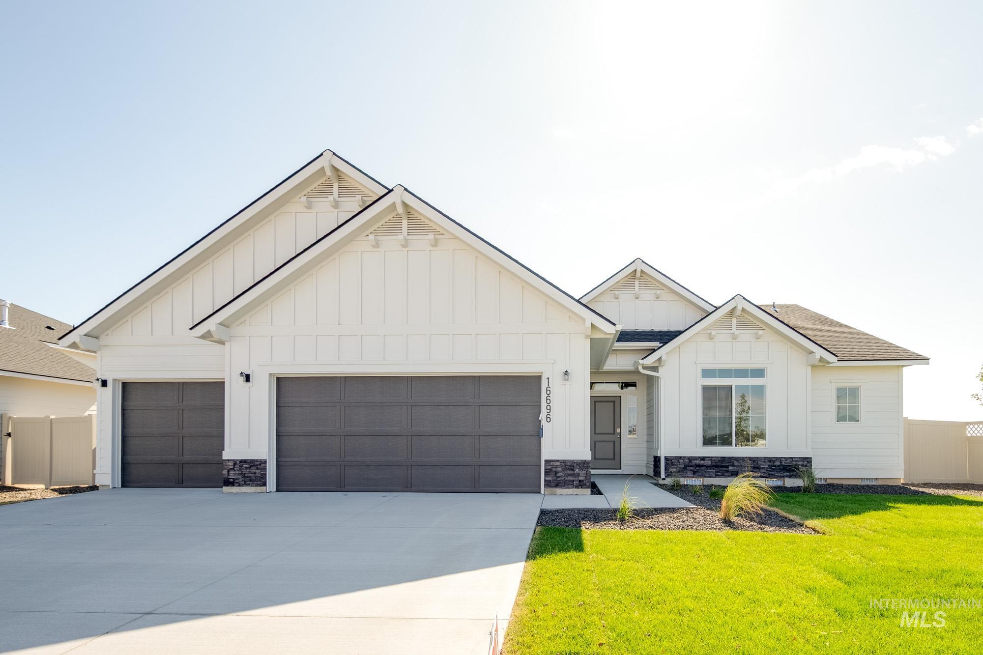 Modern farmhouse featuring board and batten siding, driveway, an attached garage, a front lawn, and stone siding