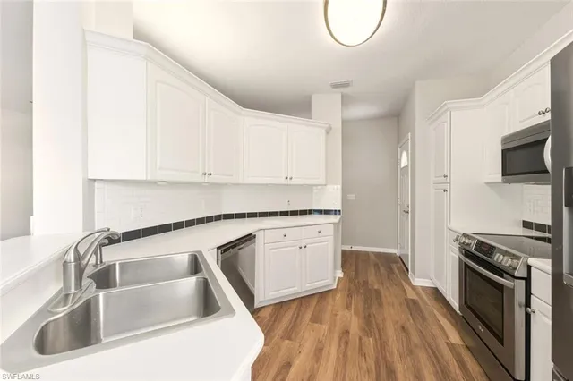 a kitchen with granite countertop a sink dishwasher stove and white cabinets with wooden floor