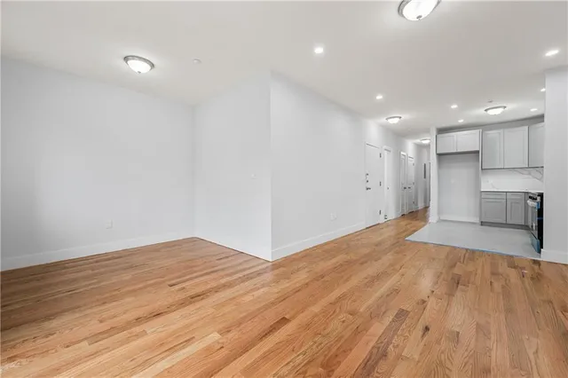 a view of empty room with wooden floor and kitchen