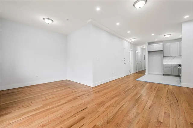 a view of empty room with wooden floor and kitchen view