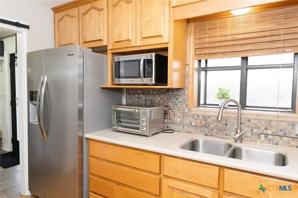 a kitchen with stainless steel appliances a sink a refrigerator a window and cabinets