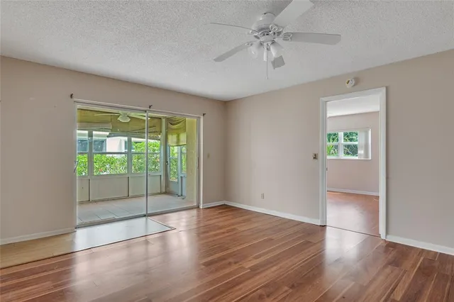 a view of an empty room with wooden floor and a ceiling fan
