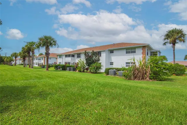 a view of a white house in front of a big yard with plants and large trees