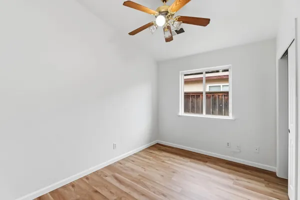 an empty room with wooden floor chandelier fan and windows
