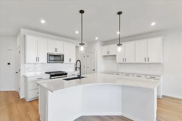 a kitchen with stainless steel appliances white cabinets a sink a stove and a wooden floors